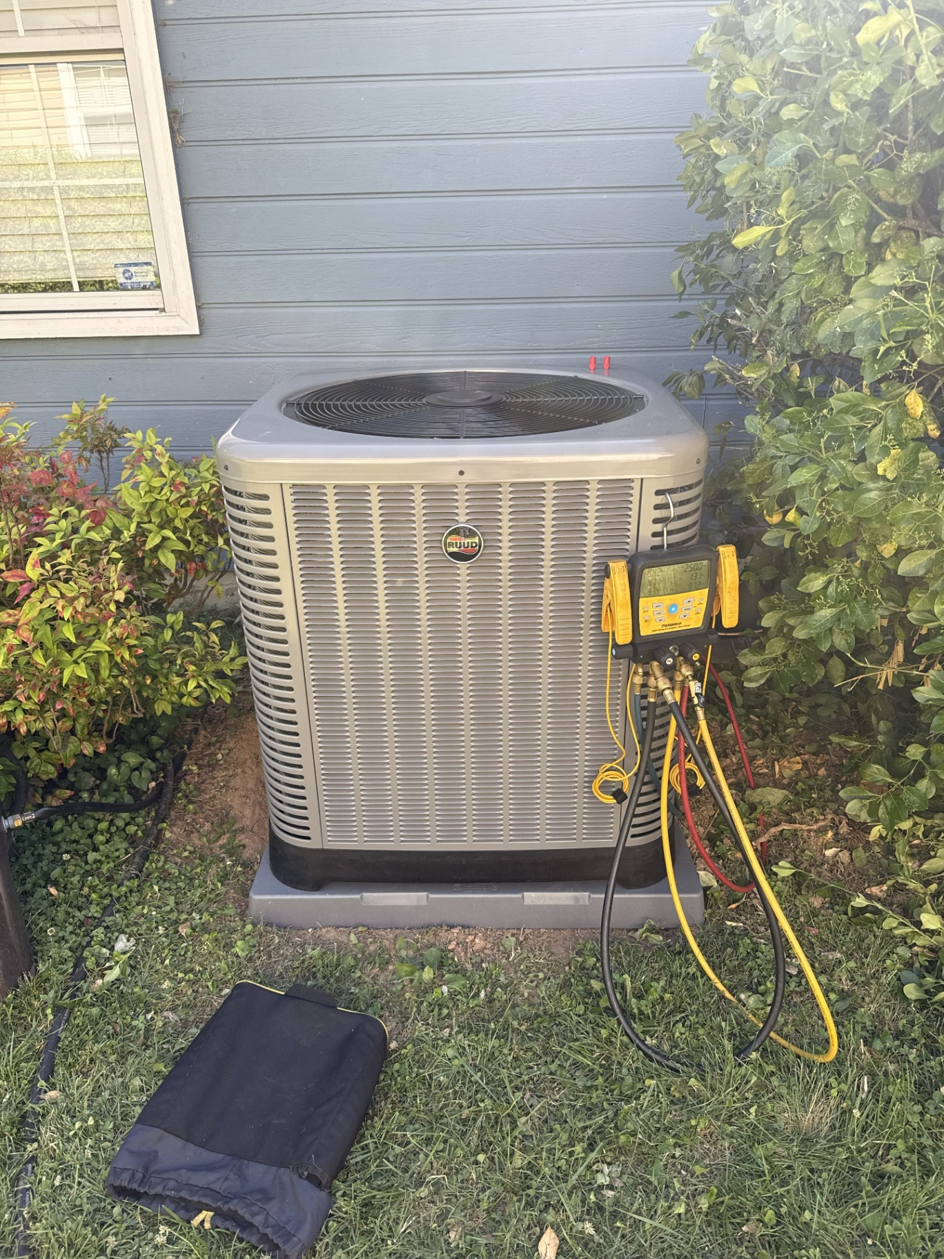 Ruud outdoor condenser being tested with digital HVAC gauges during a service visit